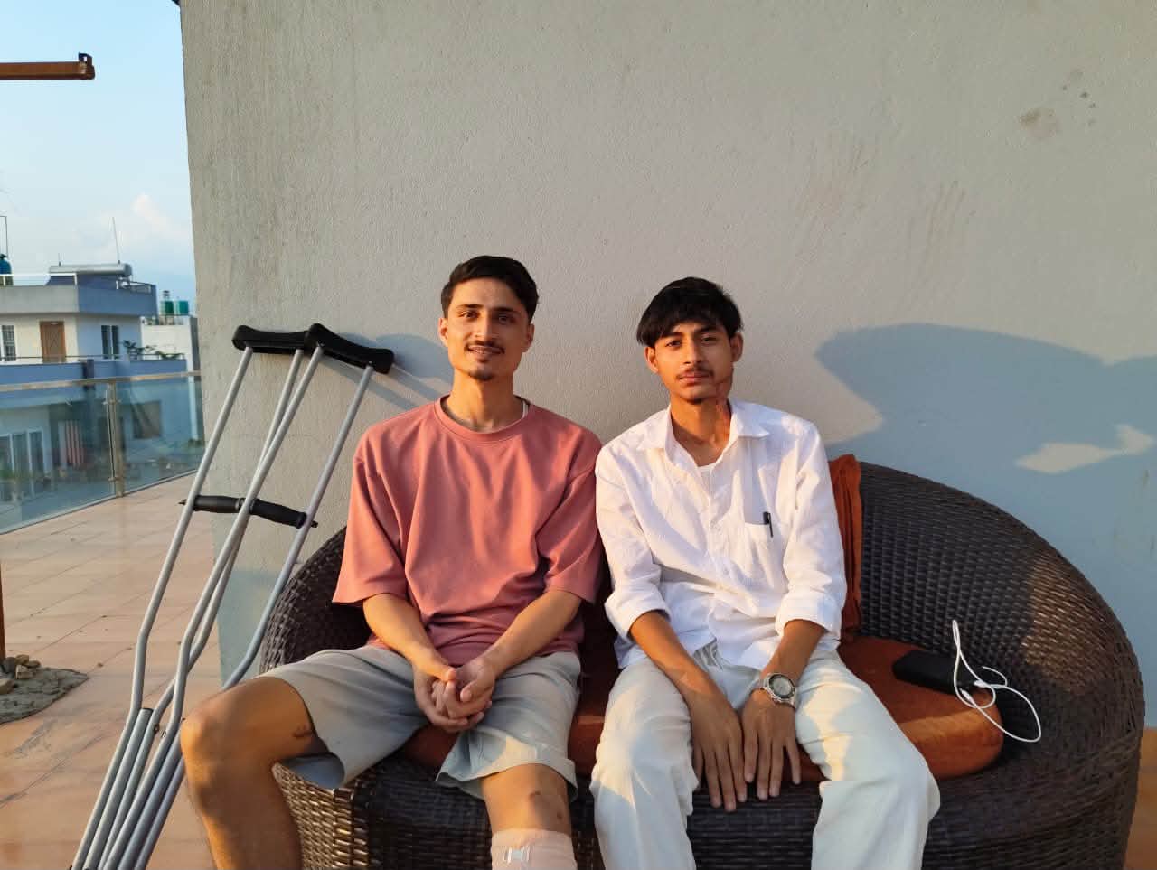 Two young men seated together with crutches nearby